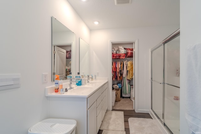 bathroom featuring wood finished floors, a sink, visible vents, double vanity, and a stall shower