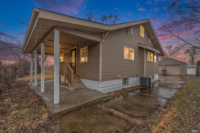 property exterior at dusk with an outbuilding, central air condition unit, covered porch, a garage, and driveway