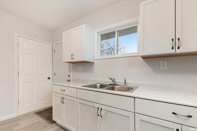 kitchen featuring light countertops, light wood finished floors, a sink, and white cabinetry