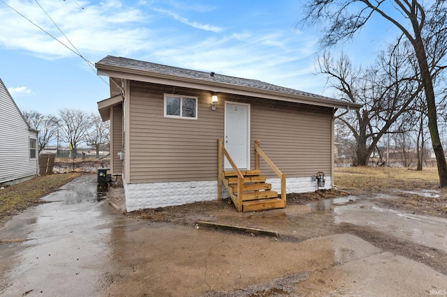 back of property with entry steps and roof with shingles