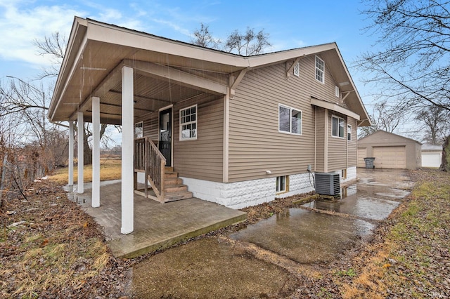 view of home's exterior featuring central AC unit, concrete driveway, a detached garage, an outbuilding, and a porch