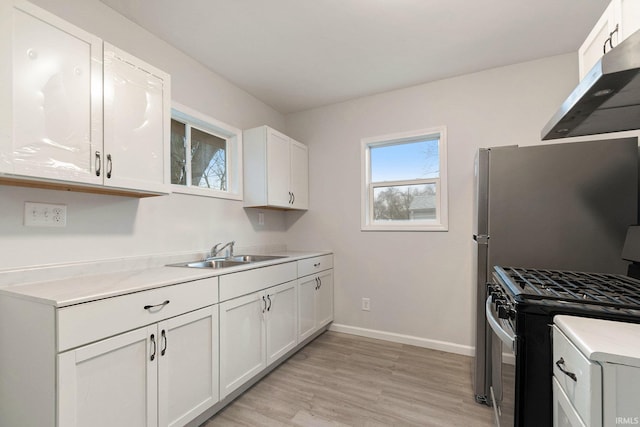 kitchen featuring light countertops, white cabinetry, a sink, stainless steel gas range, and baseboards