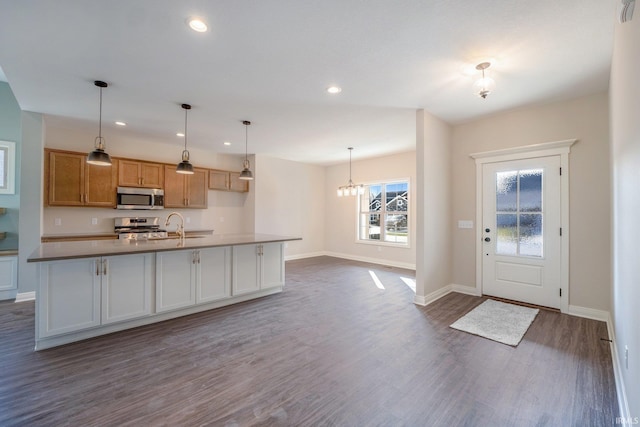 kitchen with appliances with stainless steel finishes, dark wood-style flooring, a sink, and baseboards