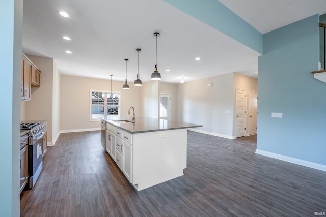 kitchen with dark wood finished floors, a center island with sink, appliances with stainless steel finishes, a sink, and baseboards