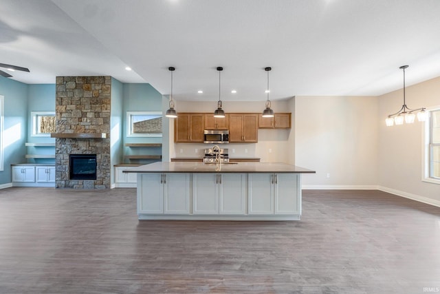 kitchen featuring a stone fireplace, wood finished floors, baseboards, open floor plan, and stainless steel microwave