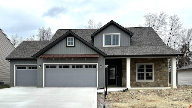 view of front facade with covered porch, concrete driveway, a shingled roof, and a garage