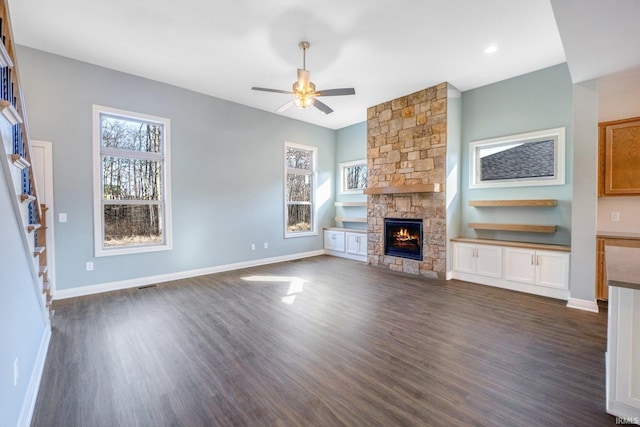 unfurnished living room featuring dark wood-style floors, a stone fireplace, baseboards, and a ceiling fan