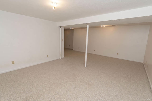 finished below grade area with light colored carpet, a textured ceiling, and baseboards