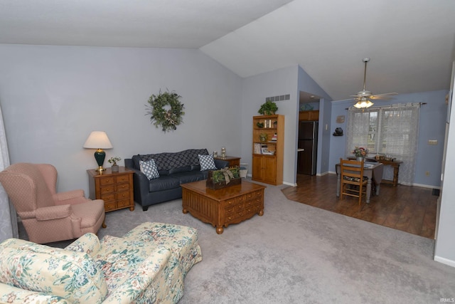 carpeted living room featuring lofted ceiling, wood finished floors, visible vents, baseboards, and a ceiling fan