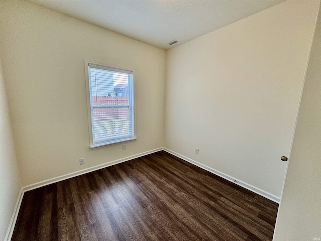 empty room with baseboards, visible vents, and dark wood-type flooring