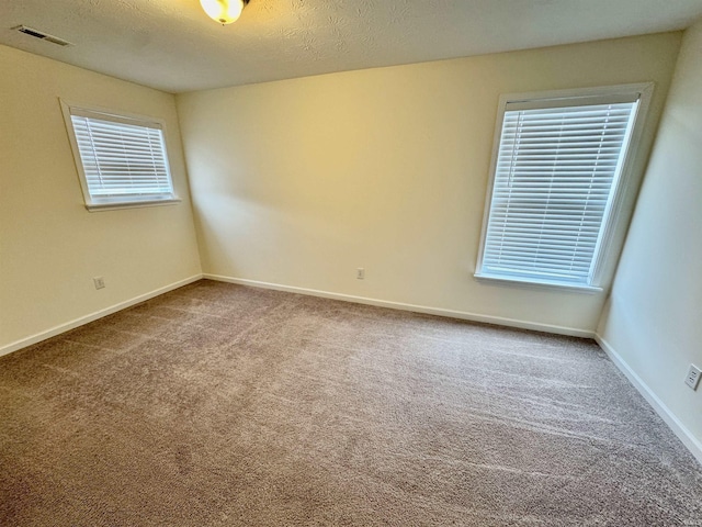 spare room with carpet floors, visible vents, a textured ceiling, and baseboards