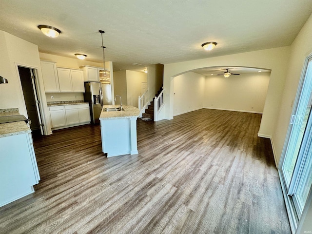 kitchen featuring a kitchen island with sink, white cabinetry, open floor plan, stainless steel refrigerator with ice dispenser, and dark wood finished floors