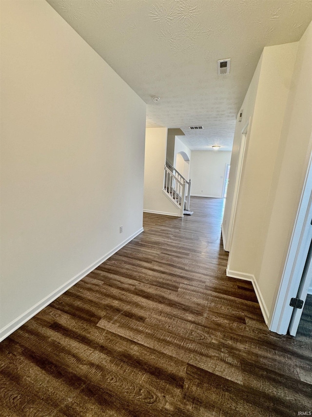 interior space with a textured ceiling, dark wood-style flooring, visible vents, baseboards, and stairs