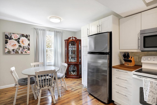 kitchen featuring baseboards, white cabinets, butcher block countertops, appliances with stainless steel finishes, and light wood-type flooring