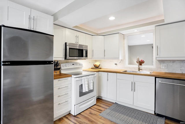 kitchen featuring light wood-style flooring, stainless steel appliances, a sink, wooden counters, and a raised ceiling