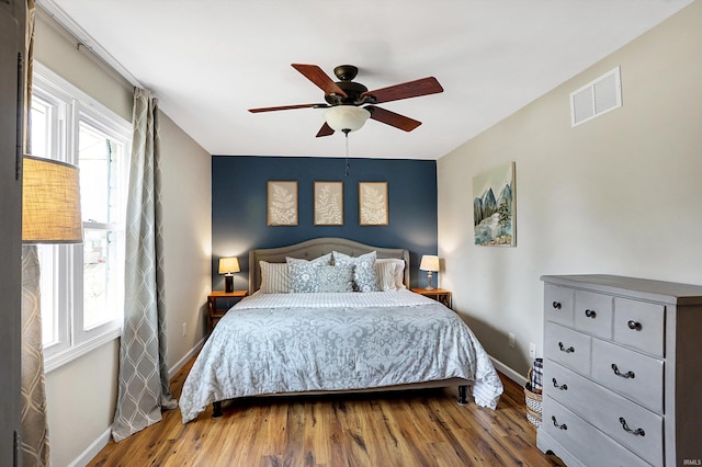 bedroom with a ceiling fan, visible vents, baseboards, and wood finished floors