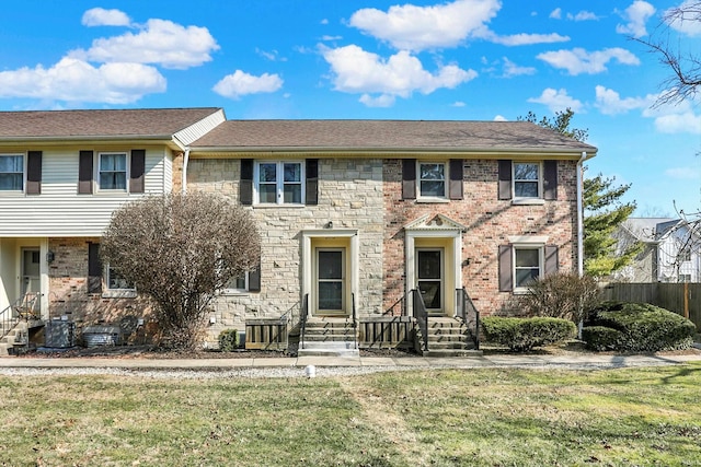 view of front facade with stone siding, roof with shingles, fence, a front yard, and brick siding