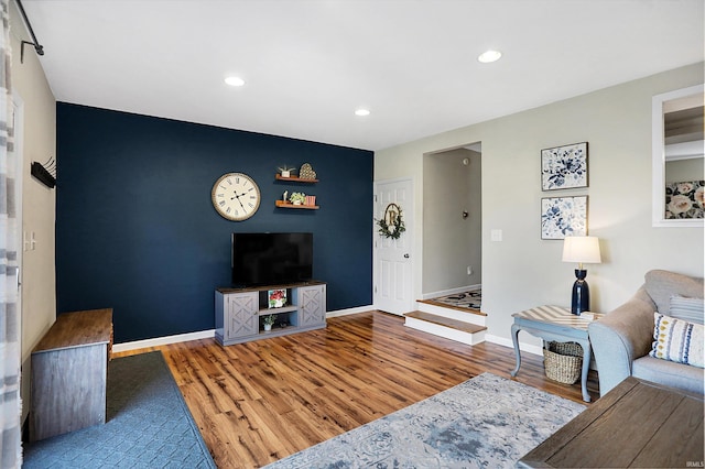 living area featuring an accent wall, baseboards, wood finished floors, and recessed lighting