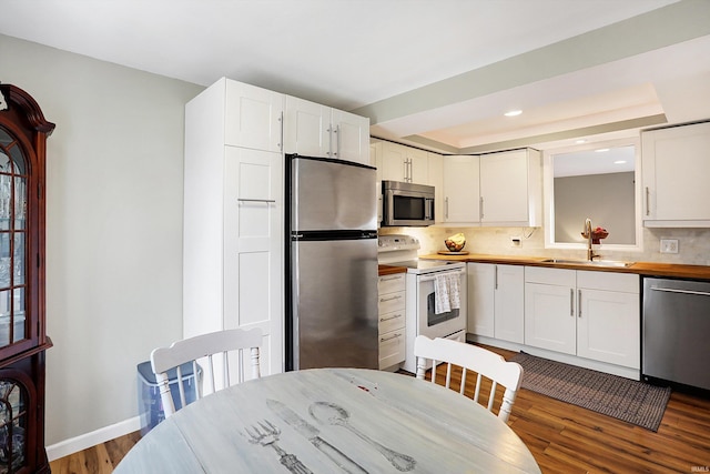 kitchen with stainless steel appliances, a sink, white cabinetry, a tray ceiling, and dark wood finished floors