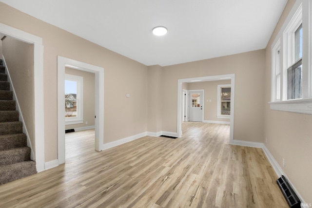 unfurnished room featuring light wood finished floors, stairway, visible vents, and baseboards