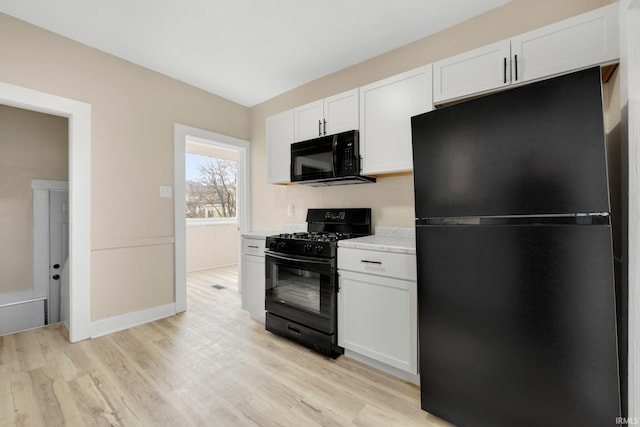 kitchen with light countertops, light wood-style flooring, white cabinetry, black appliances, and baseboards