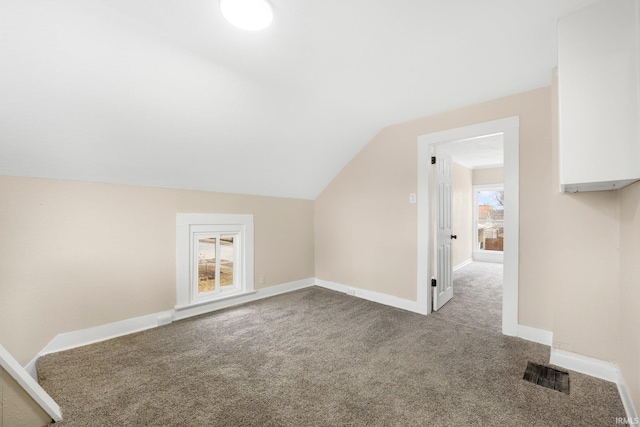 additional living space with baseboards, visible vents, vaulted ceiling, and carpet flooring