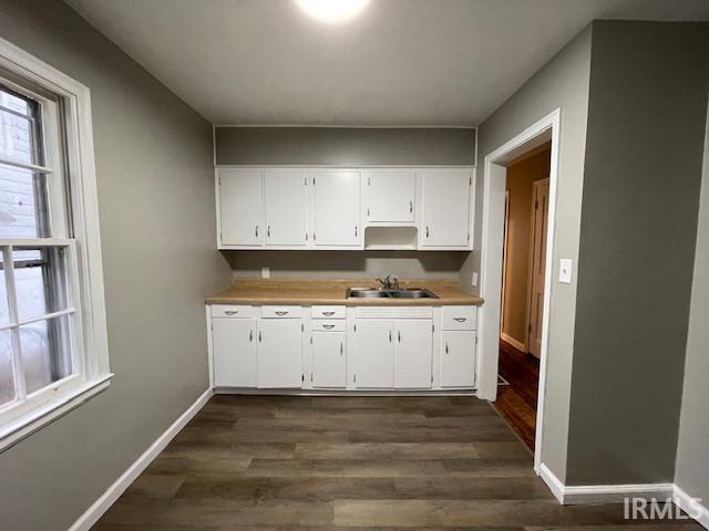 kitchen with a sink, baseboards, white cabinets, light countertops, and dark wood-style floors