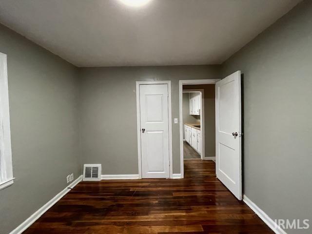 unfurnished room featuring dark wood-style flooring, visible vents, and baseboards