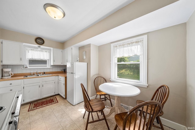 kitchen with backsplash, freestanding refrigerator, white cabinetry, a sink, and baseboards