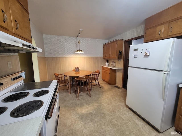 kitchen with light floors, brown cabinetry, wood walls, white appliances, and under cabinet range hood