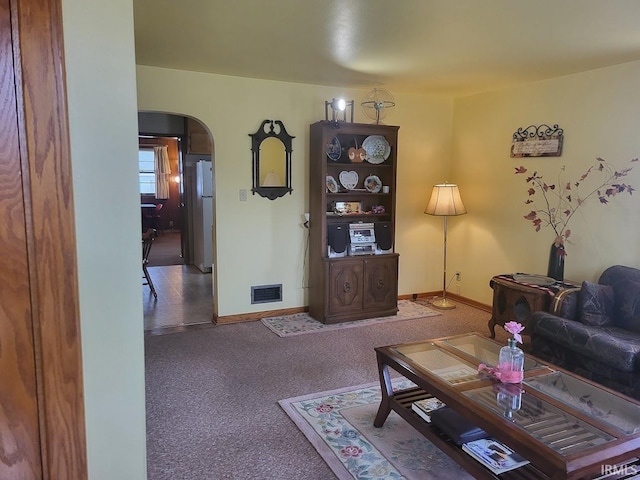 carpeted living area featuring arched walkways, visible vents, and baseboards