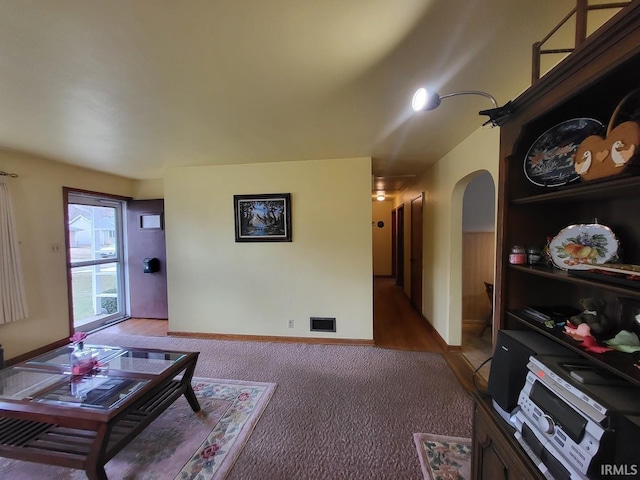 carpeted living area featuring arched walkways, visible vents, and baseboards