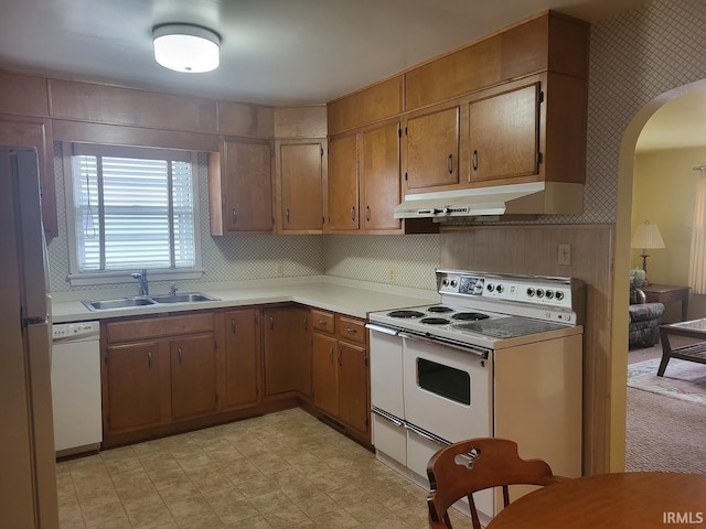 kitchen featuring arched walkways, under cabinet range hood, white appliances, a sink, and light countertops