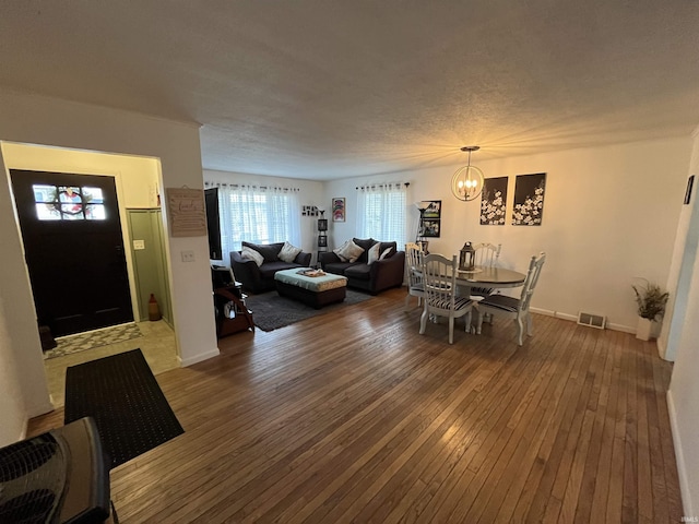 dining area with a textured ceiling, hardwood / wood-style flooring, a notable chandelier, visible vents, and baseboards