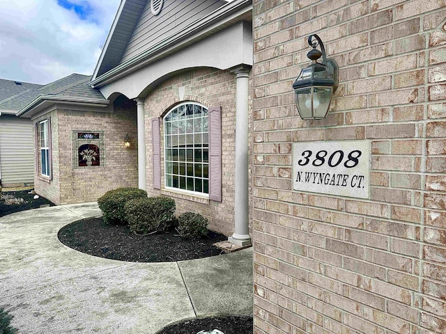 doorway to property featuring a shingled roof and brick siding