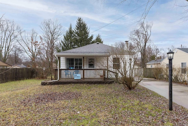 bungalow-style home featuring covered porch, a shingled roof, and fence