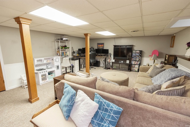 living room featuring carpet floors, a wainscoted wall, a drop ceiling, and decorative columns