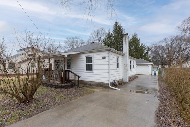 view of front of house featuring a garage, driveway, a shingled roof, a chimney, and an outdoor structure