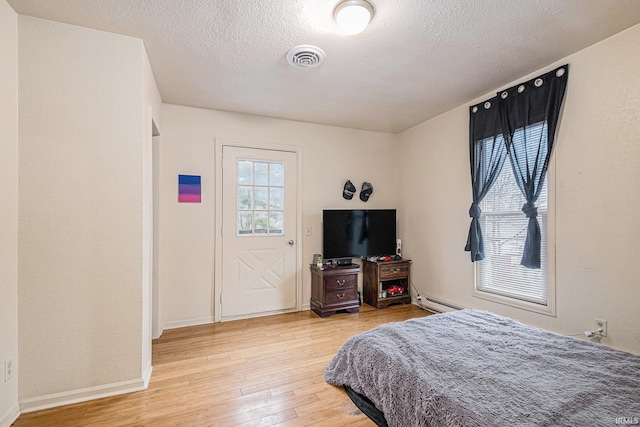 bedroom featuring visible vents, baseboard heating, a textured ceiling, light wood-type flooring, and baseboards