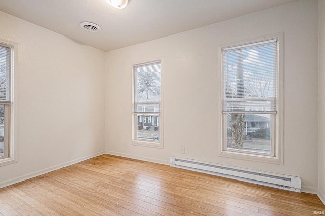 spare room with light wood finished floors, visible vents, a baseboard heating unit, and baseboards