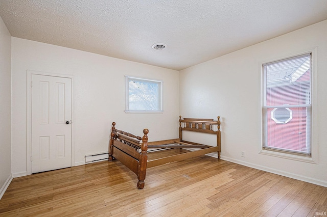 living area featuring a textured ceiling, light wood-style flooring, visible vents, baseboards, and baseboard heating