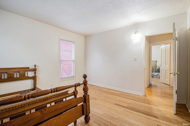 bedroom with light wood finished floors, baseboards, and a textured ceiling