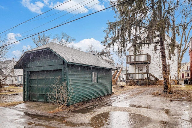 view of side of home featuring roof with shingles, a detached garage, driveway, and an outdoor structure