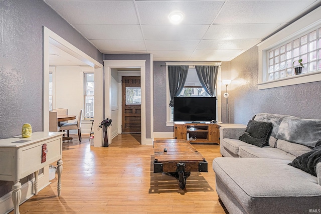 living room with baseboards, a textured wall, a paneled ceiling, and light wood-style floors