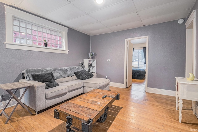 living room featuring a textured wall, light wood finished floors, a paneled ceiling, and baseboards