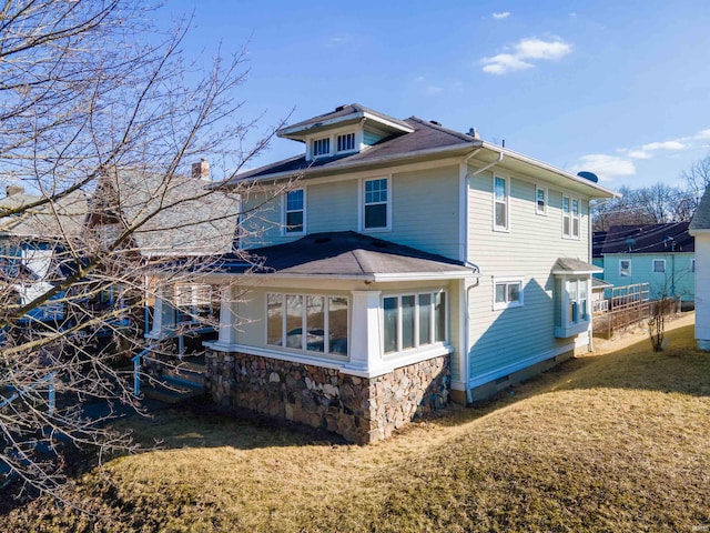 back of house with stone siding and a yard