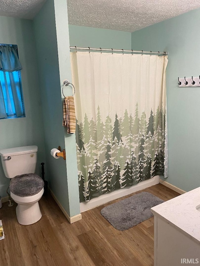 full bathroom with toilet, a shower with shower curtain, a textured ceiling, wood finished floors, and baseboards