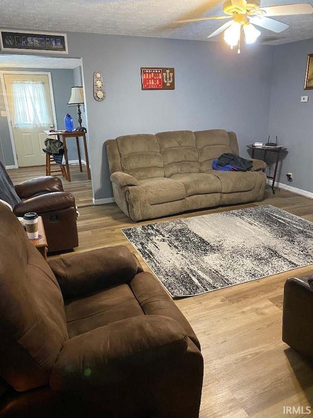 living area featuring a textured ceiling, wood finished floors, a ceiling fan, and baseboards