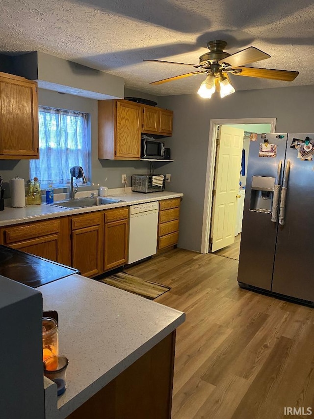 kitchen with brown cabinets, a sink, light wood-type flooring, stainless steel fridge, and dishwasher