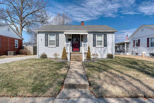 bungalow-style home featuring brick siding, a chimney, a front yard, and cooling unit